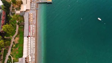 Huzurlu sahil manzarası. Berrak turkuaz sular güneşli bir gökyüzünün altında güneşli yataklar ve ahşap iskele ile kaplı kumlu kıyılarla buluşur..