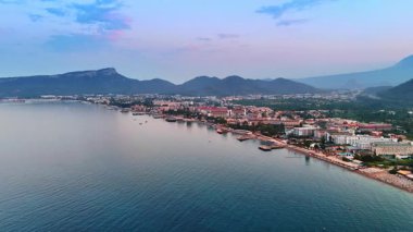 Sahildeki bir tatil köyünün manzarası. Gün batımında bir sahil beldesinin manzarası, bereketli dağları ve teknelerle dolu sakin bir denizi gösteriyor..