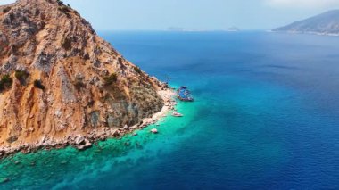 Tekneler dev kayanın etrafındaki çapanın üzerinde duruyor. Türkiye 'deki Akdeniz' in çarpıcı masmavi su manzarası üzerindeki İHA görüntüleri.
