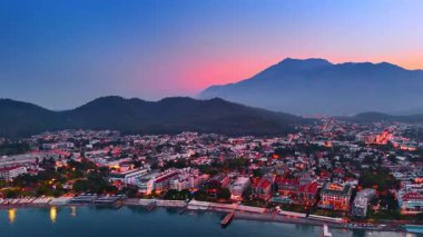 Günbatımında Türkiye 'nin Fethiye kentindeki modern tatil beldesinin renkli manzarasına yaklaşıyoruz. Arkaplanda, dağların ardında pembe gökyüzü..