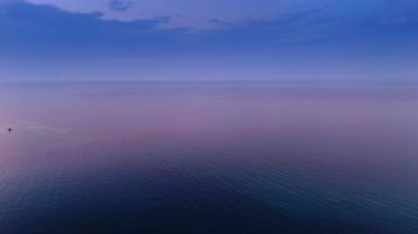 Gün batımında sonsuz deniz manzarası pembeye boyanır. Suya küçük bir ışık yansıyor..