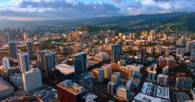 Modern Honolulu 'nun geniş şehir manzarası dağların yeşil yamaçlarına ve vadiye saçıldı. Batan güneş şehrin bir kısmını aydınlatıyor. Yağmur bulutları manzaranın üzerinde gökyüzünde toplanır. Hawaii, ABD.