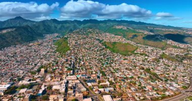 Modern Honolulu, Hawaii, ABD 'nin yoğun olarak inşa edilmiş kentsel alanının güneşli manzarası. Arka plandaki yoğun bulutların altında inanılmaz yeşil dağ sıraları var. Hava görünümü.