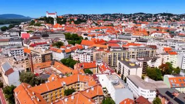 Turuncu çatıları olan güzel tarihi binaların üzerinde uçuyorlar. Arkaplanda yeşil tepedeki Bratislava Kalesi.