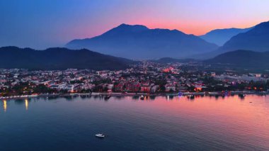 Türkiye 'nin Kemer kıyılarına gün batımında ışıklar açık olarak daha yakın uçuyor. Pembe ışık suları boyuyor ve dağların arkasındaki gökyüzünü..