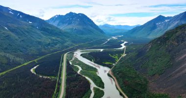 Dallanan nehir boyunca uzanan otoyol vadide akıyor. Nehrin deltası, çarpıcı kayaların arasında. Alaska doğası tepeden bakıldığında.