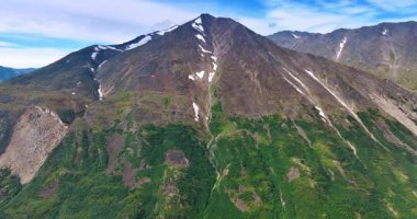 Büyük dağların yamaçlarında küçük kar yatar. Yeşillik tarafından yarı kapalı kayaya yaklaşıyoruz. Alaska vahşi doğası.