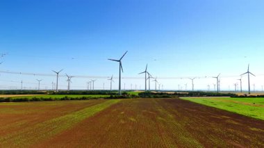 Rüzgar türbinleri temiz enerji üretir. Rüzgâr türbinleri açık mavi gökyüzünün altında yeşil bir çiftlik arazisinin üzerinde dimdik durur ve yenilenebilir enerjiyi iş başında gösterir..