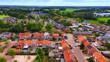 Parlak banliyö sahnesi, öğleden sonra. Yeşil çimenleri, kırmızı çatıları ve öğleden sonra aydınlığında dolambaçlı yolları olan canlı bir banliyö manzarası..