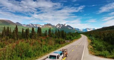Minibüsle hızlı bir uçuş. Binası olan bir yere yaklaşıyoruz. Arka planda nefes kesen dağlar. Alaska doğası.