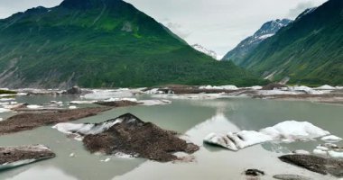 Nehrin üzerinden buz parçalarıyla uçmak. Arkaplanda muhteşem yeşil dağlar var. Alaska vahşi doğası.