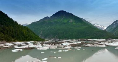 Buz parçaları nehirden sarkmış. Arkaplandaki büyük yeşil dağa yaklaşıyoruz. Alaska manzarası.