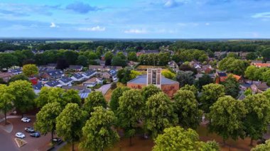 Overloon, Hollanda 'daki Theobalduskerk' e yaklaşan İHA görüntüleri. Gündüz vakti köyün yeşil renkli yerleşim yerinin manzarası.