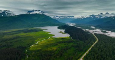 Görkemli dağların arasında nehir olan görkemli bir vadi. Manzaranın üstündeki gri bulutlu gökyüzü. Hava görüntüsü. Alaska vahşi doğası.