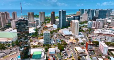Çok sayıda araba park etmiş ve güneşli bir şehrin manzarasının yanından geçiyor. Ayna yüzlü, gökdelenin yakınındaki görüntüler. Honolulu, Hawaii, ABD.
