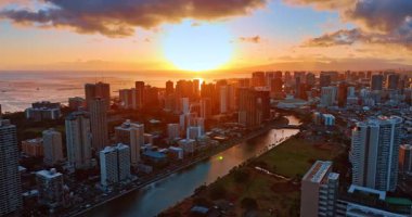Honolulu, Hawaii, ABD 'deki Waikiki tatil köyüne yaklaşıyoruz. Günbatımının turuncu ışığı manzarayı kaplıyor. Hava görünümü.