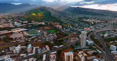 Honolulu, Hawaii, ABD şehir merkezinden geçen yollar sistemi. Otoyolda birden fazla araba hareket ediyor. Güneş ışığı yeşil dağları aydınlatır. Hava görünümü.