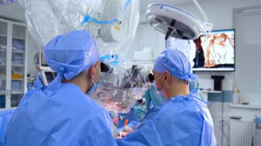 Karmaşık ameliyatlarda cerrahlar. Mavi cerrahi kıyafetli iki cerrah modern bir ameliyathanede ileri teknolojiyi kullanarak hassas bir prosedüre odaklanıyorlar..