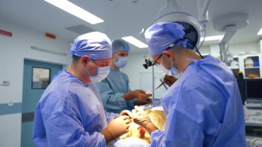 Cerrahlar ameliyathanede ameliyat eder. İki cerrah hassas bir operasyon gerçekleştirirken hemşire de iyi donanımlı bir cerrahi ortamda yardımcı oluyor..