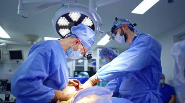 Cerrahlar. Önlük ve maske takmış iki cerrah, parlak ve modern bir ameliyathanede cerrahi bir operasyon gerçekleştiriyor..