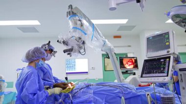 Cerrahlar ileri seviyede ameliyat yaparlar. Mavi önlüklü doktorlar robot aletler ve monitörlerle karmaşık bir ameliyat yapıyorlar..