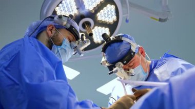 Cerrahlar hastanede ameliyat yaparlar. Mavi önlüklü iki cerrah bir ameliyathanede karmaşık bir cerrahi prosedüre odaklanıyor..