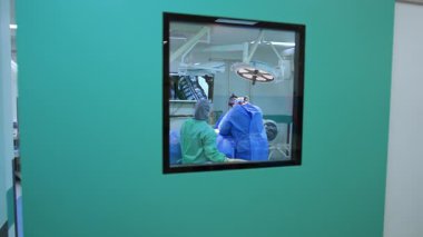 Cerrahlar ameliyatta. Cerrahi kıyafetli iki cerrah, iyi aydınlatılmış bir ameliyathanede tıbbi bir prosedür sırasında bir hastaya odaklanıyor..