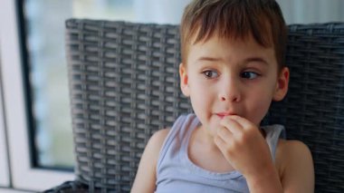 Güneşli bir günde çerez yiyen bir çocuk. Genç bir çocuk, rahat bir ortamın sıcak güneşinin tadını çıkarırken, bir sandalyede oturup atıştırmanın tadını çıkarıyor..