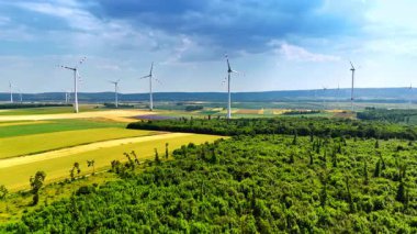 Türbinler yeşil alanda yükseliyor. Rüzgâr türbinleri yeşil alanlar ve ormanlar üzerinde yükseliyor, canlı kırsal alanlarda yenilenebilir enerjiyi vurguluyor.
