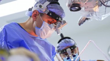 Ameliyat sırasında ameliyat masasında ameliyat maskesini takan beyaz erkek cerrah. Mikroskop mercekleri hastanın üstünde. Düşük açı. Beyin cerrahisi.