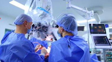 İşbirliği yapan cerrahların arka görüntüsü. Beyin cerrahları mikroskoba bakıyorlar. Beyin ameliyatı yapıyorlar..