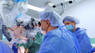 Profesyonel erkek beyin cerrahı mikroskoba bakar. Doktor modern aletleri beyin cerrahisinde uyguluyor. Çalışanlara yardım ediyorum..