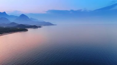 Alacakaranlıkta pembeye boyanmış güzel sakin su manzarası. Kıyıdaki dağ siluetleri. Hava perspektifi.