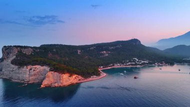 Akdeniz 'in cennet gibi kayalık yeşil kıyısına yaklaşıyoruz. Yatlar su yüzeyinde. Gün batımında gökyüzü ve deniz pembesi. Kemer, Türkiye.