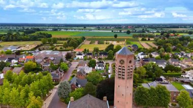 Hollanda kırsalının havadan görünüşü. Yeşil tarlaların havadan görünüşü, büyüleyici evler ve kırsal alanda canlı bir gökyüzünün altında bir kule..