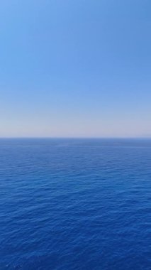 Sonsuz mavi okyanus berrak gökyüzüyle buluşur. Geniş okyanus berrak bir gökyüzü altında uzanır, uzak dağlar sakin kıyı manzarasına eklenir..