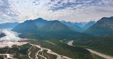Bulutlu gökyüzünün altındaki şaşırtıcı yeşil kayalık manzara. Vadideki nehirler ve dağ eteğindeki büyük buzullar. Alaska manzarası. Hava görünümü.