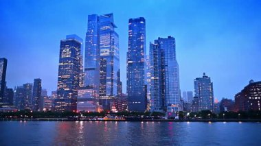 Gökdelenler ve gökdelenler alacakaranlıkta ışıkları yaktılar. ABD, New York 'un çarpıcı modern mimarisine nehir manzarasından düşük açılı bakış açısı.