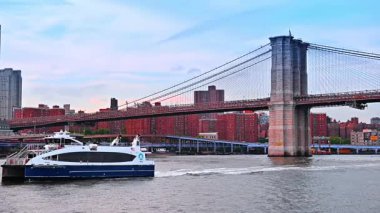 Beyaz ve mavi nehir teknesi Doğu Nehri 'nin su manzarasında yavaşça ilerliyor. New York, ABD 'deki Brooklyn Köprüsü' nün alçak açılı görüntüsü.