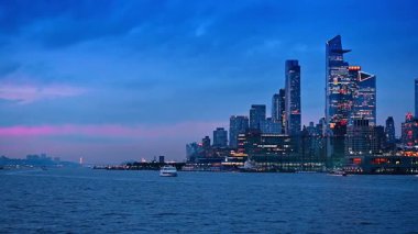 Beyaz nehir teknesi su manzarasından kameraya yaklaşıyor. Alacakaranlıkta New York, ABD 'nin inanılmaz modern silueti.