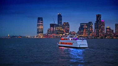 New York, ABD 'deki nehir teknesiyle akşam seyahati. Çok katlı binalar ve gökdelenler arka plandaki ışıkları açtı.