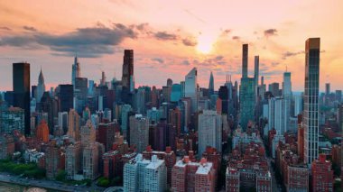 Manhattan 'a doğu nehrinin yukarısından yaklaşıyor. Arkaplanda gün batımında turuncu gökyüzü. New York manzaralı İHA görüntüleri.