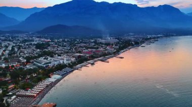 Birçok insan Akdeniz 'in sahil sınırında dinleniyor. Türkiye 'nin Kemer tatil beldesinde gün batımında manzara. Arkaplanda büyük kayalar.