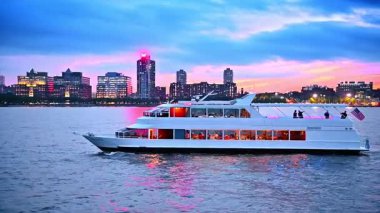 Nehir teknesi alacakaranlıkta insanları nehir kıyısına taşıyor. Arka planda New York 'un parlak silueti.