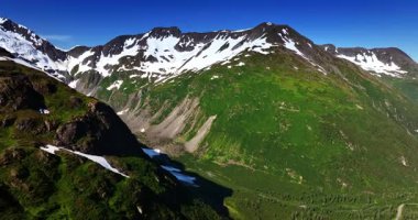 Yamaçlarda çimlerle, tepelerde karla kaplı muhteşem dağlar. Parlak güneş Alaska 'daki dağları aydınlatıyor. Hava görünümü.