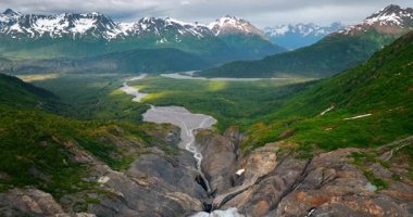 Alaska 'nın vahşi doğasında karla kaplı muhteşem dağlar. Kayaların üzerinde, ayaklarında bir nehirle..