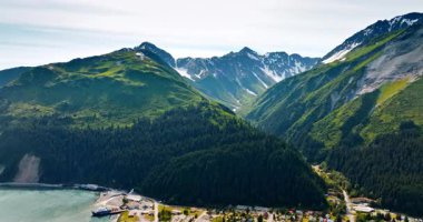Evergreen çam ağacı ağaçları muhteşem dağların yamaçlarını kaplar. Nehrin yanındaki dağın eteğinde bir kasaba bulunmaktadır. Alaska havadan görünüyor..