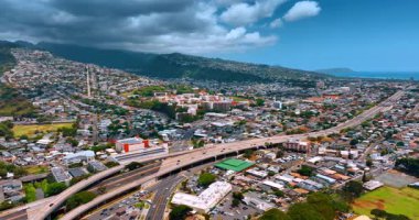 Modern Honolulu 'nun yoğun kentsel manzarası işlek otoyol ile kesişiyor. Yerleşim alanı olan yeşil dağlar gri bulutlarla kaplıdır. Hava görünümü.