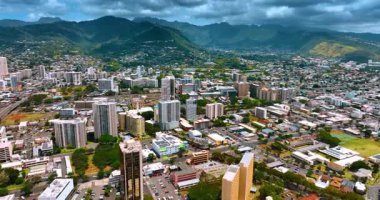 Modern Honolulu manzarası, Hawaii, ABD. Yamaçlarda evleri olan yeşil dağlara yaklaşıyorlar. Gökyüzünde dramatik bulutlar.