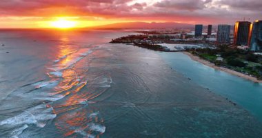 Gün batımında geniş dalgalar kıyıya vurur. Arka planda gökyüzünde güzel turuncu güneş. Hawaii kıyıları, ABD hava sahası.